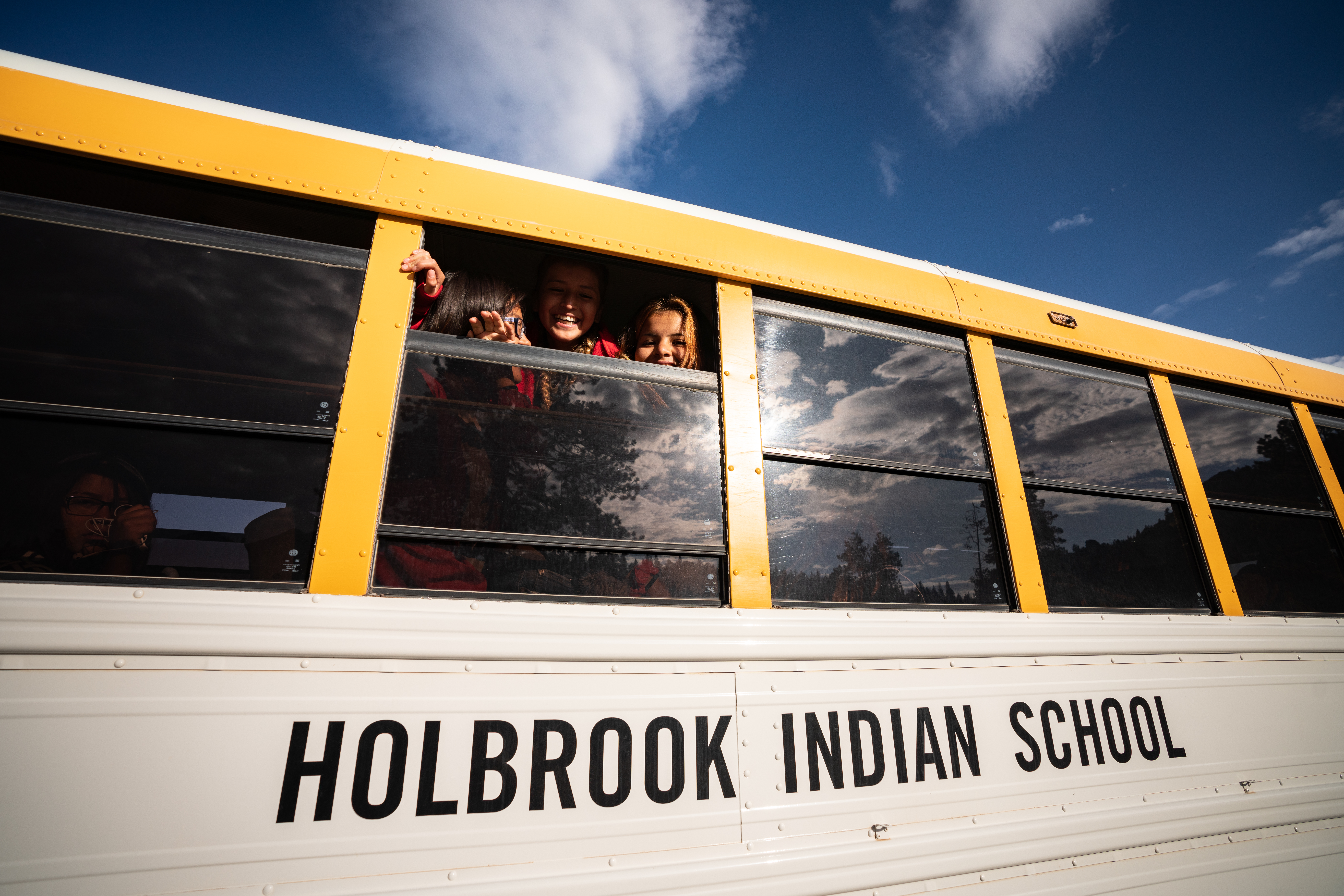 Students of Holbrook Indian School smile from the window of a school bus. 