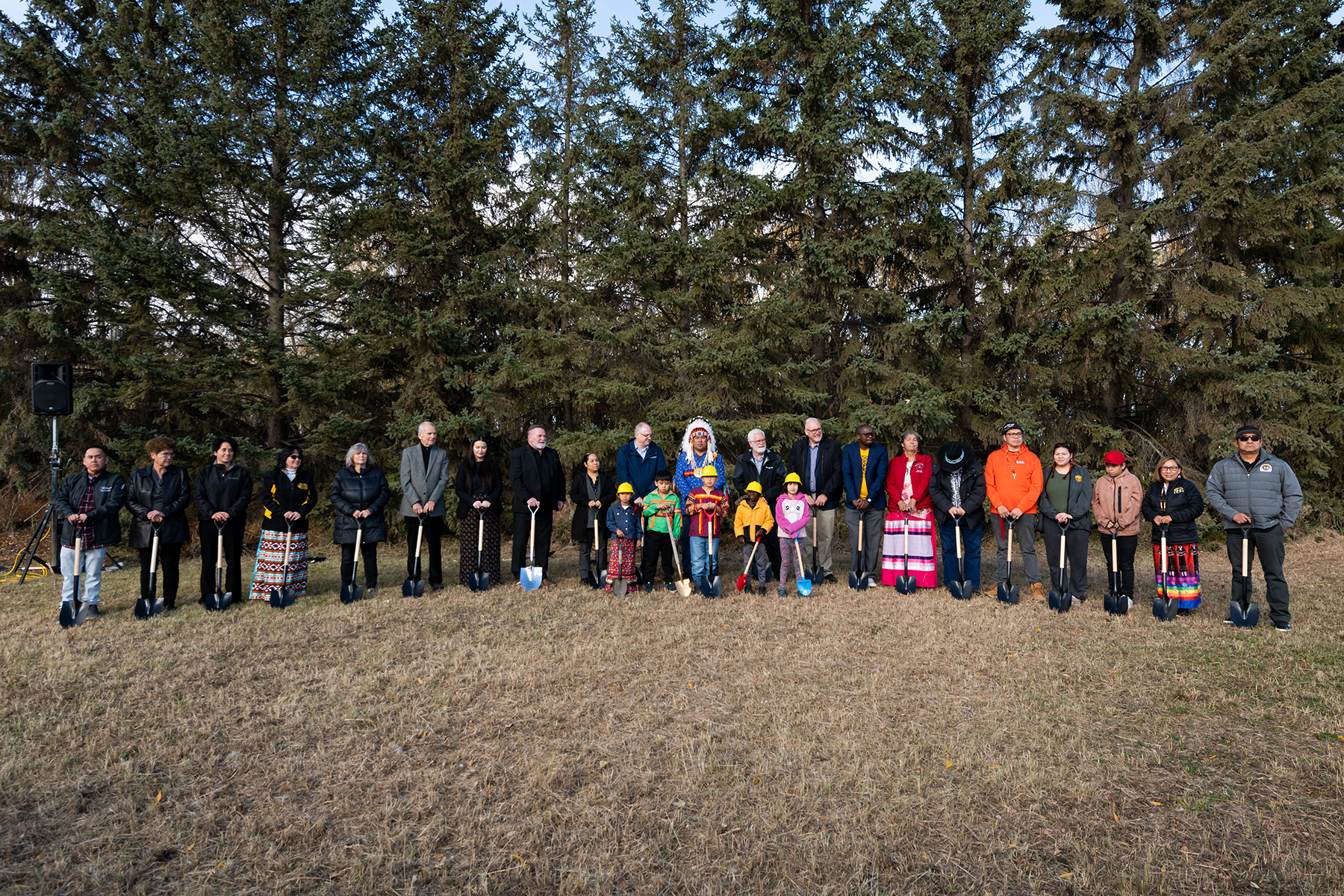 Several people stand together on an empty field as part of a groundbreaking ceremony. 