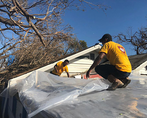 ACS volunteers lay a tarp over an exposed home. 