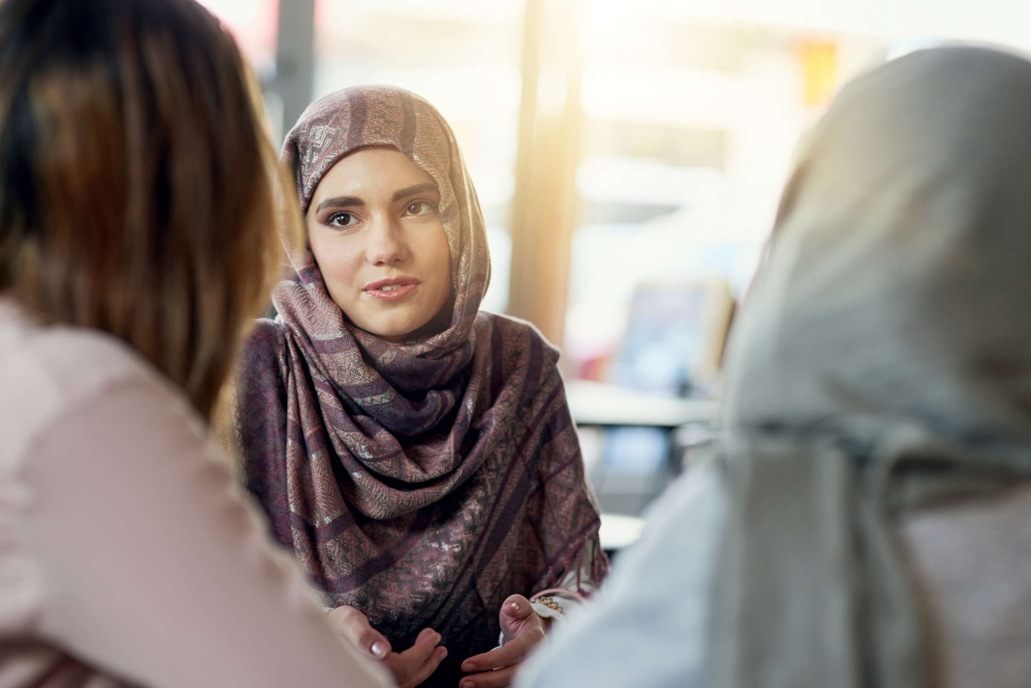 stock photo of two Muslim women talking to third women
