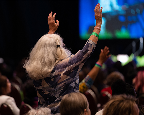 Convention attendee stands and lifts her hands in response to praise and worship. 
