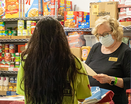 Young student speaking to older woman standing in a food pantry