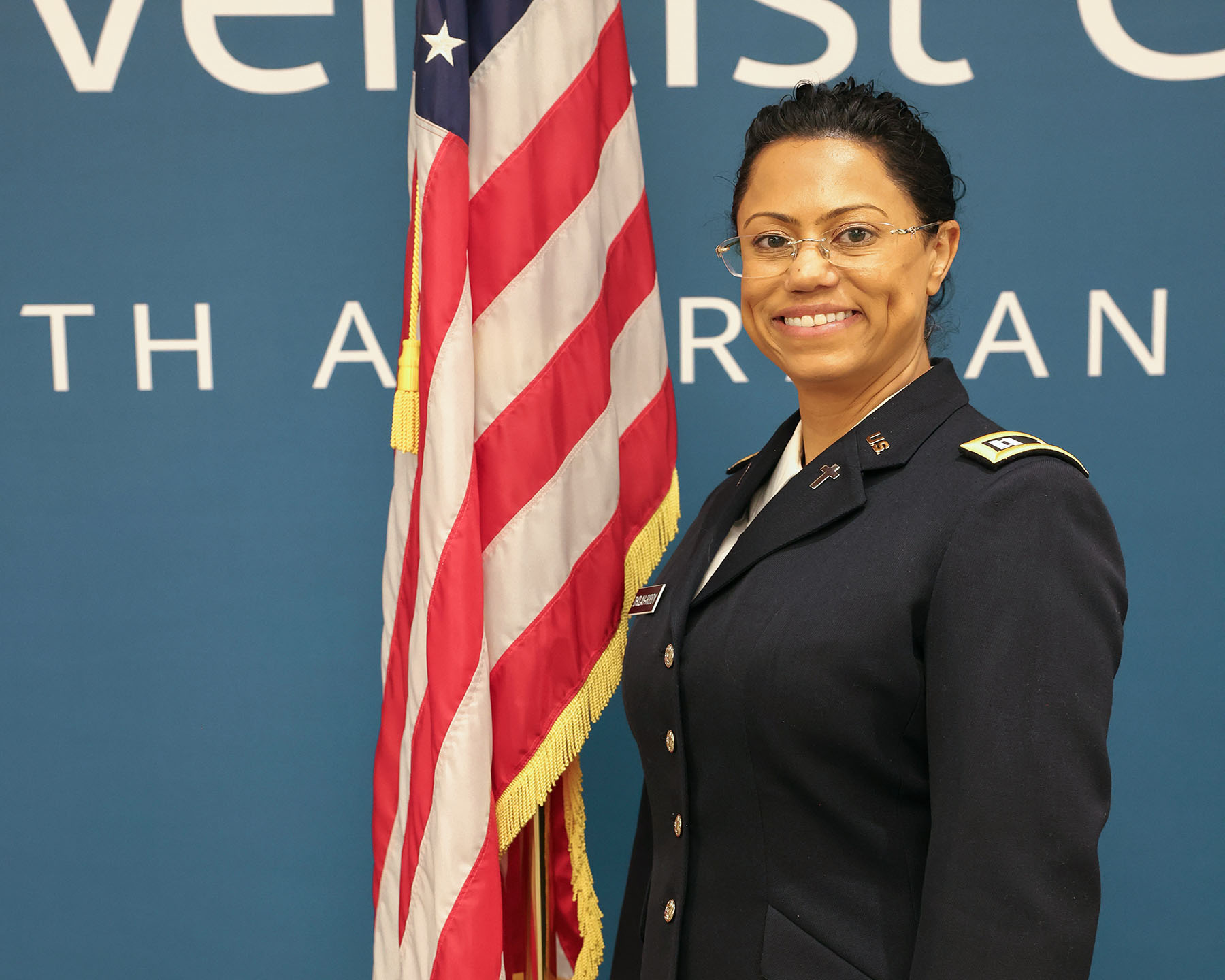 Woman in uniform smiling next to American flag.
