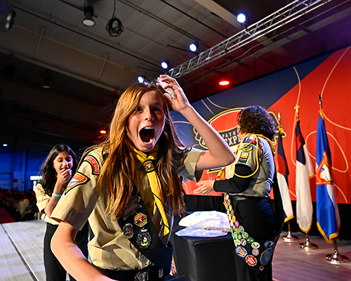 Happy young woman in a Pathfinder uniform receiving an award. Another young woman and leader are in the background. 