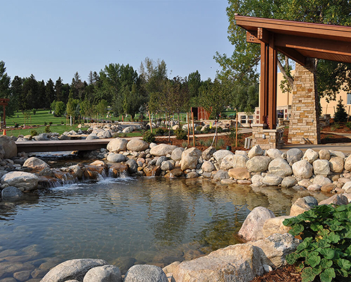 Photo of a man-made river surrounded by rocks and trees, with part of a building visible. 