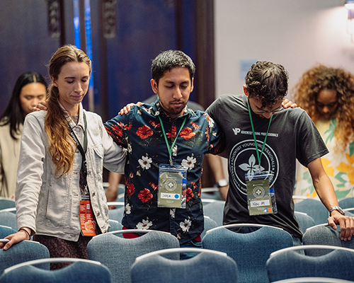 Three young adults bow their heads during prayer at the 2024 Adventist Young Professionals conference