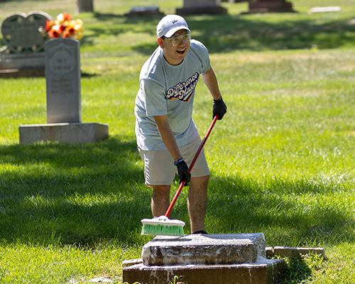 Middle age white man cleans a headstone at IPC community service clean up in local cemetery