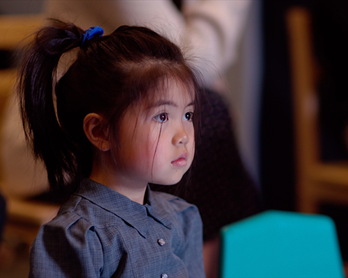 Asian toddler girl watches a screen intently in classroom setting