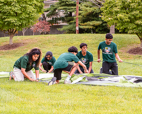 Young people putting up a tent on a grassy plain