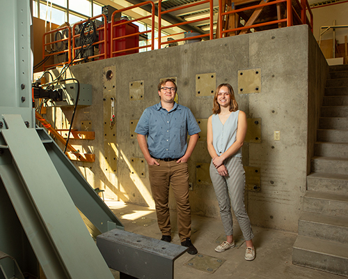 A young man and woman stand in an engineering lab amid building structures. 