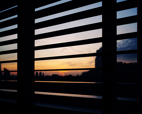 screen shot of cityscape at dusk as seen through the blinds on a window