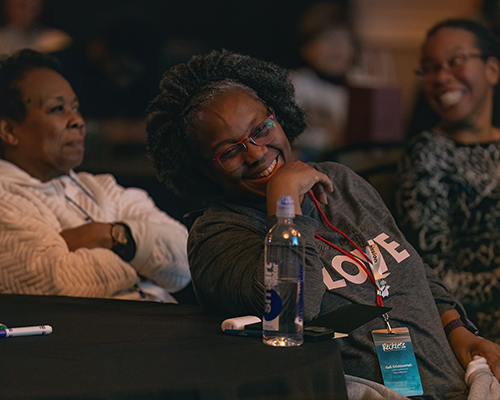 Close-up of three black women laughing and smiling at a table.