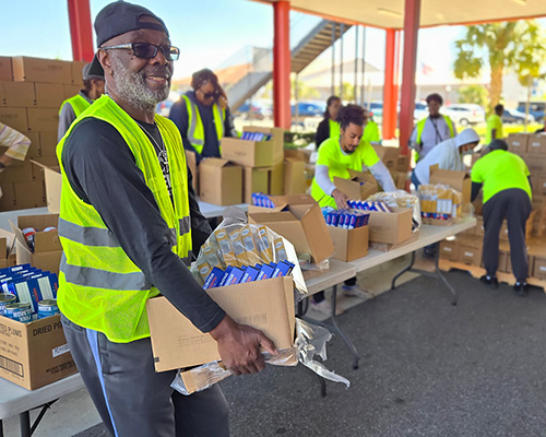 Black man wearing a yellow safety vest working at a food distribution site