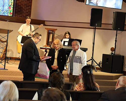 A pastor gives a gift to an elderly couple at the front of a church.