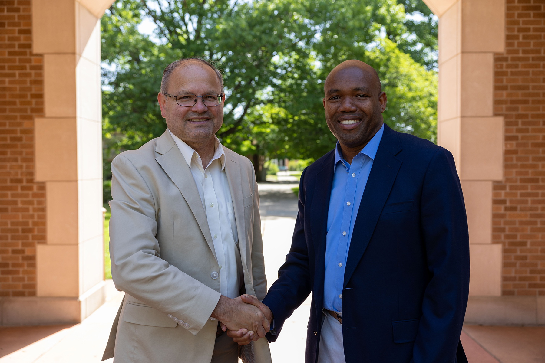 Two men of different ethnicities smiling and shaking hands.