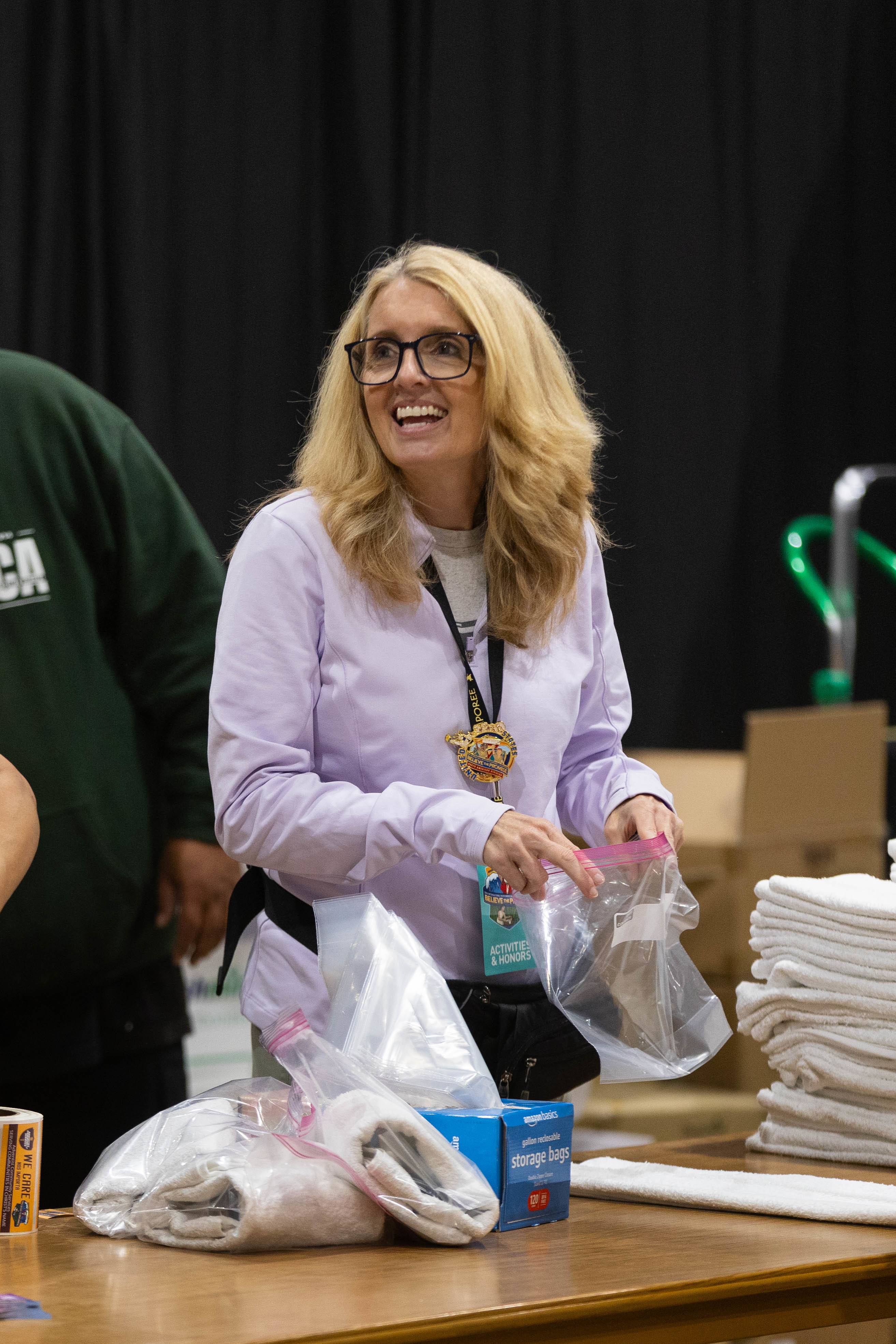     A smiling woman with a Ziploc bag in her hand puts together a hygiene kit for the community. 