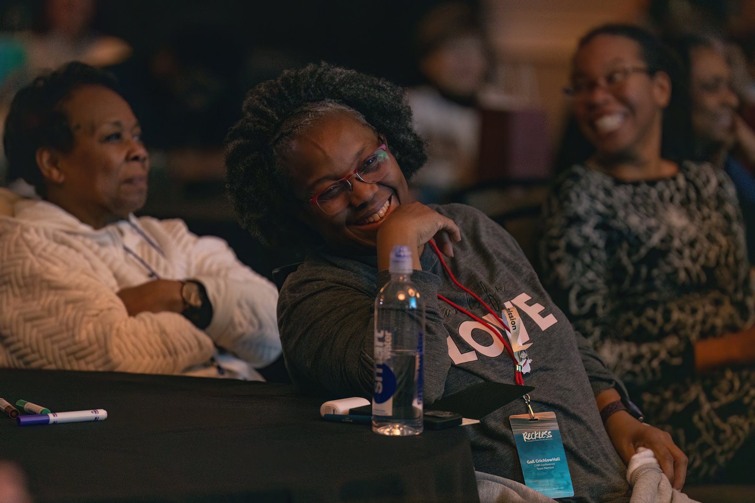 Three black women pictured laughting and smiling at a table. 