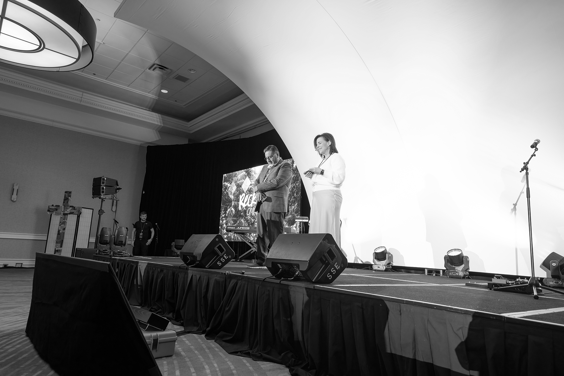 Black and white photo of a man and woman praying on a stage.