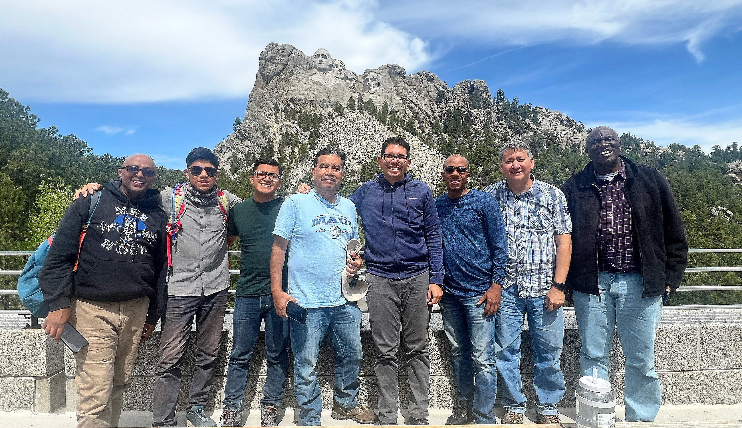 a diverse group of men stand in front of Mount Rushmore