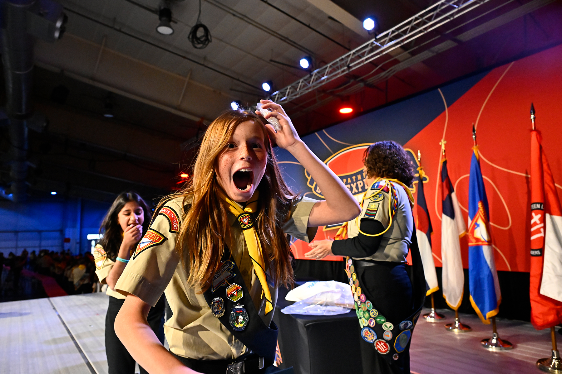 A young girl in a Pathfinder uniform looking thrilled after picking up an award. Another girl and leader in the background.