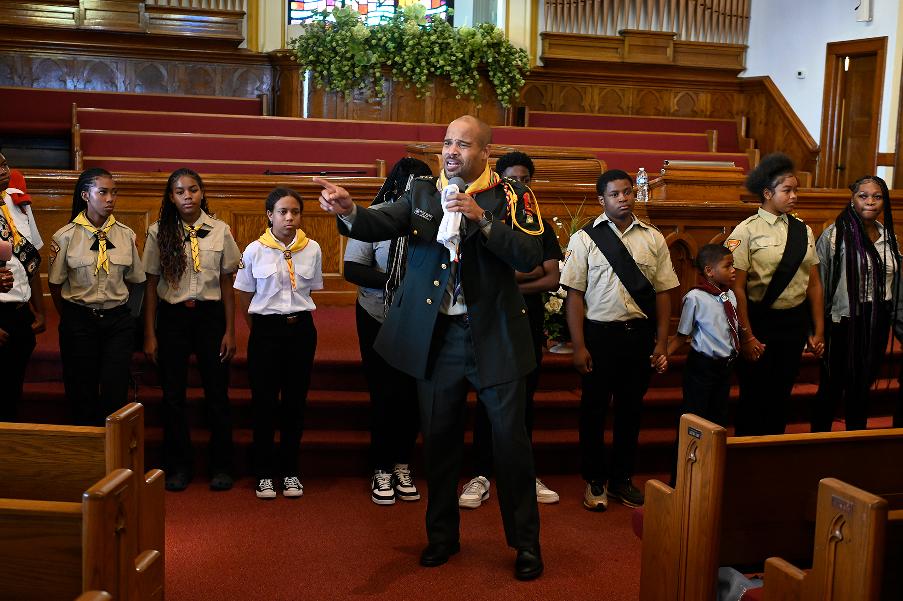 photo of a pastor speaking at the front of a church, looking animated, with Pathfinders behind him.