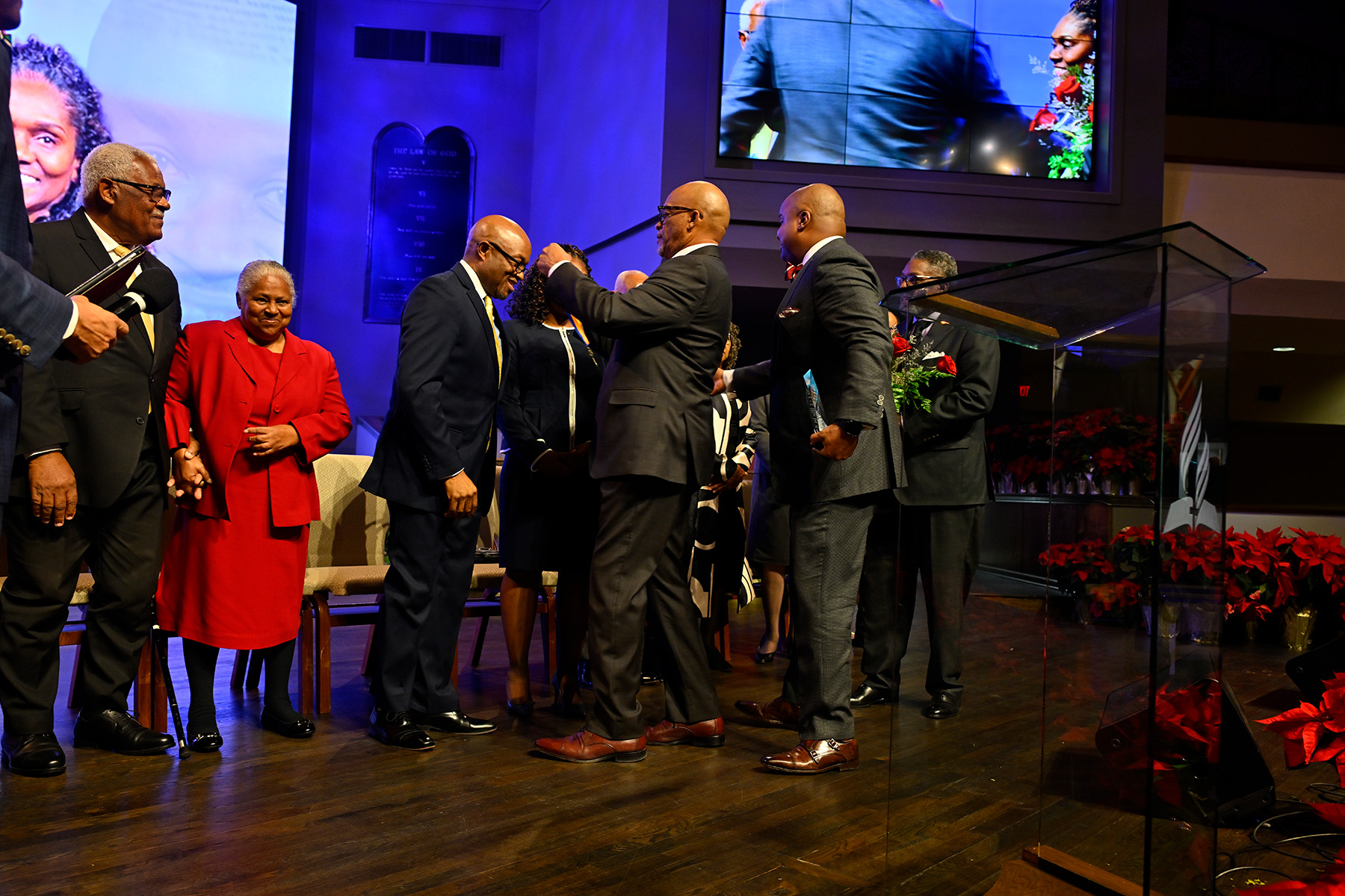 A man stands on stage, smiling, as another man presents him with a medallion. His wife, other honorees, and program organizers, are also on stage. 