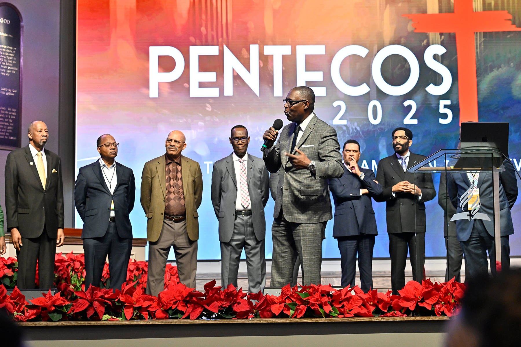 Several men, one speaking in the middle, stand in front of a banner reading "Pentecost 2025."