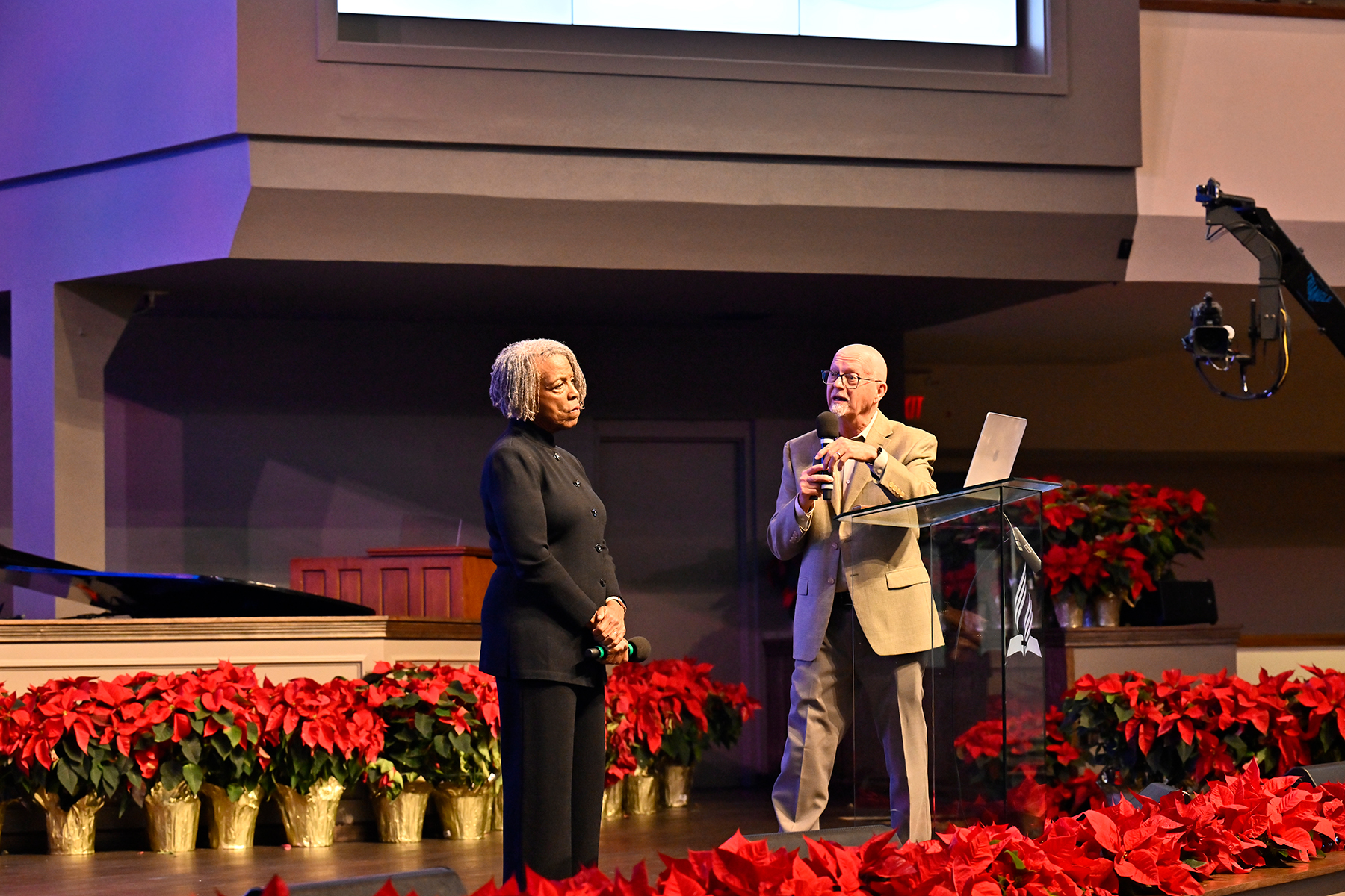 A black woman and white man speak at the front of a room. 