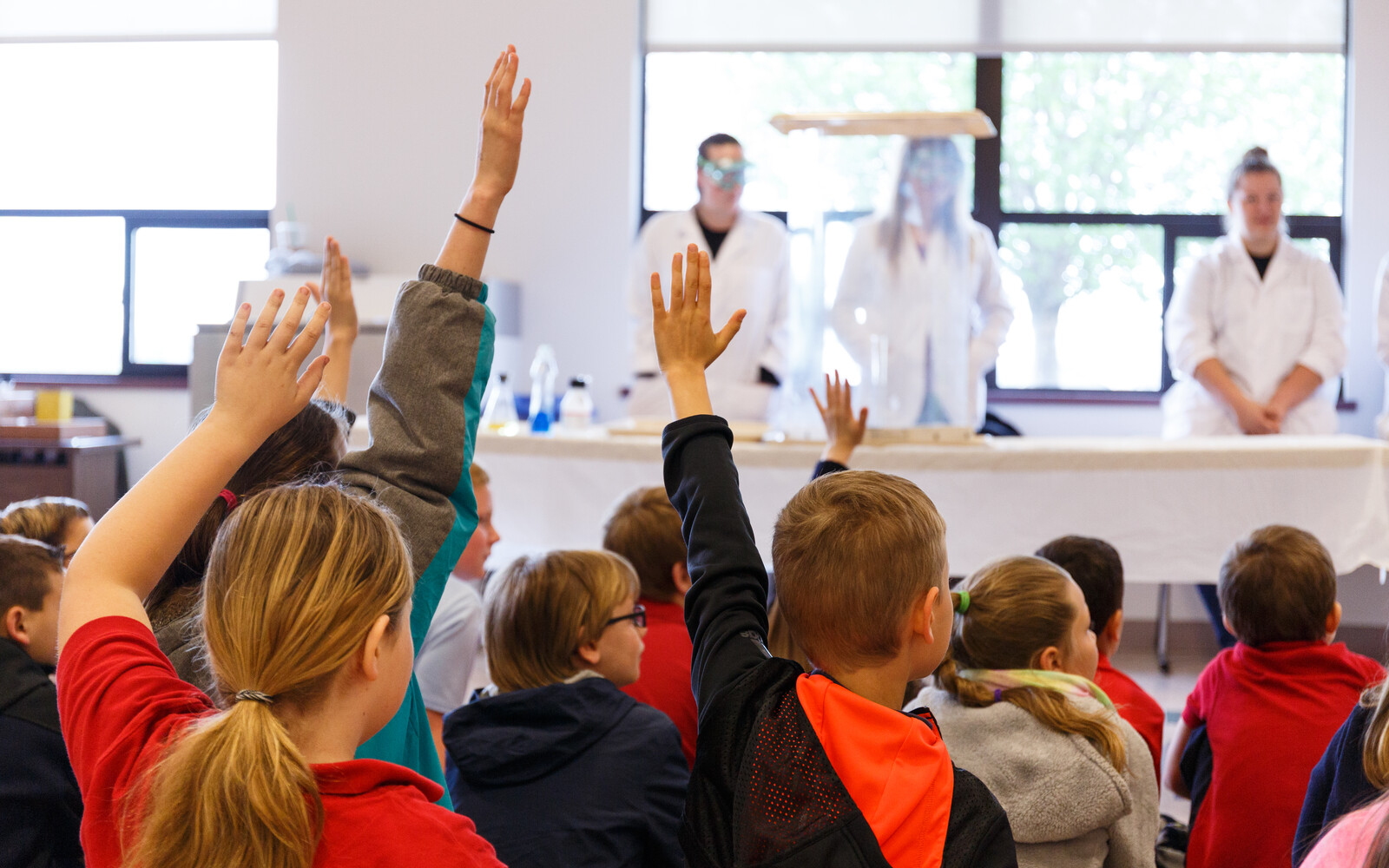 A back shot of children in a classroom raising their hands