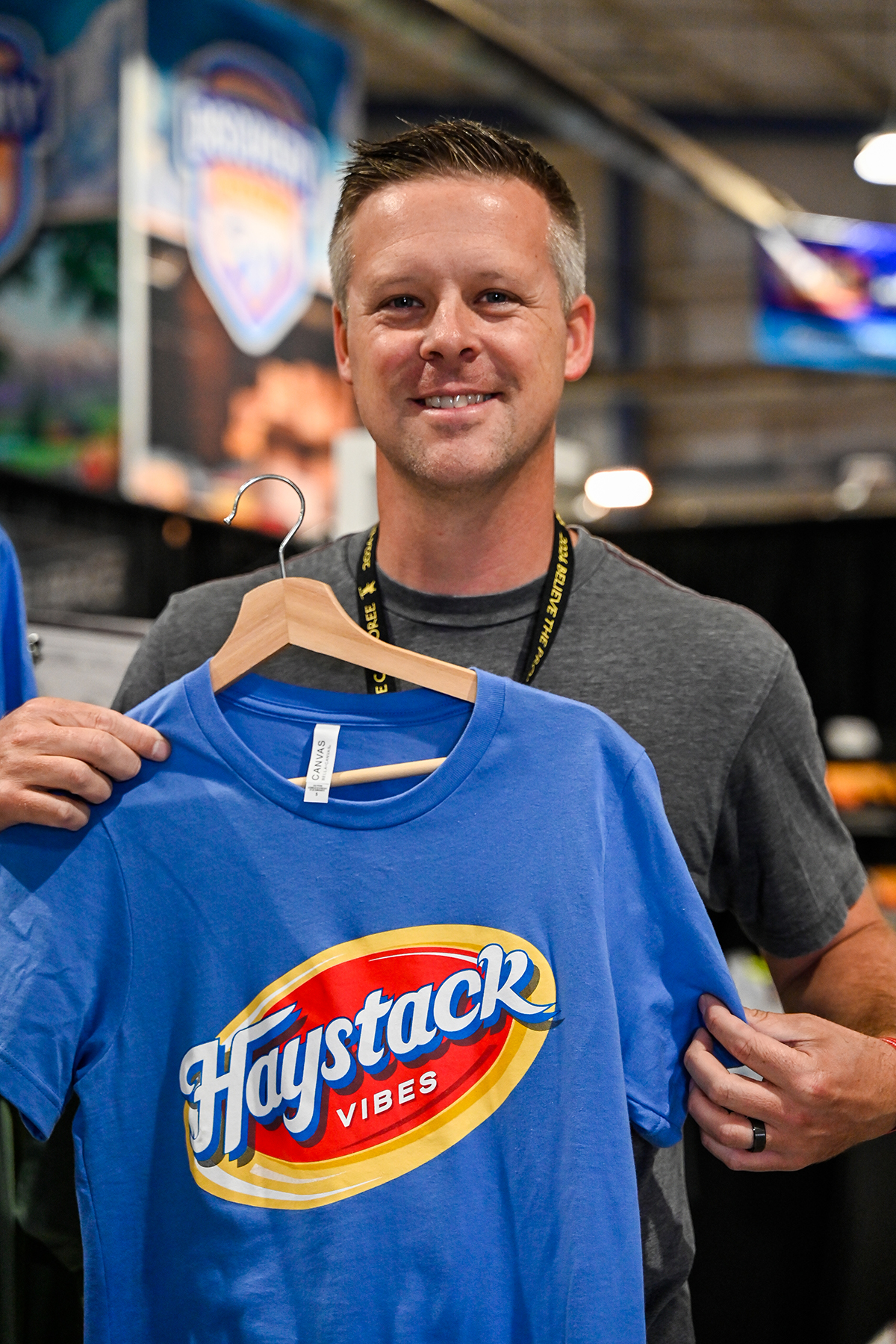 picture of a smiling man holding a shirt that reads "Haystack vibes."