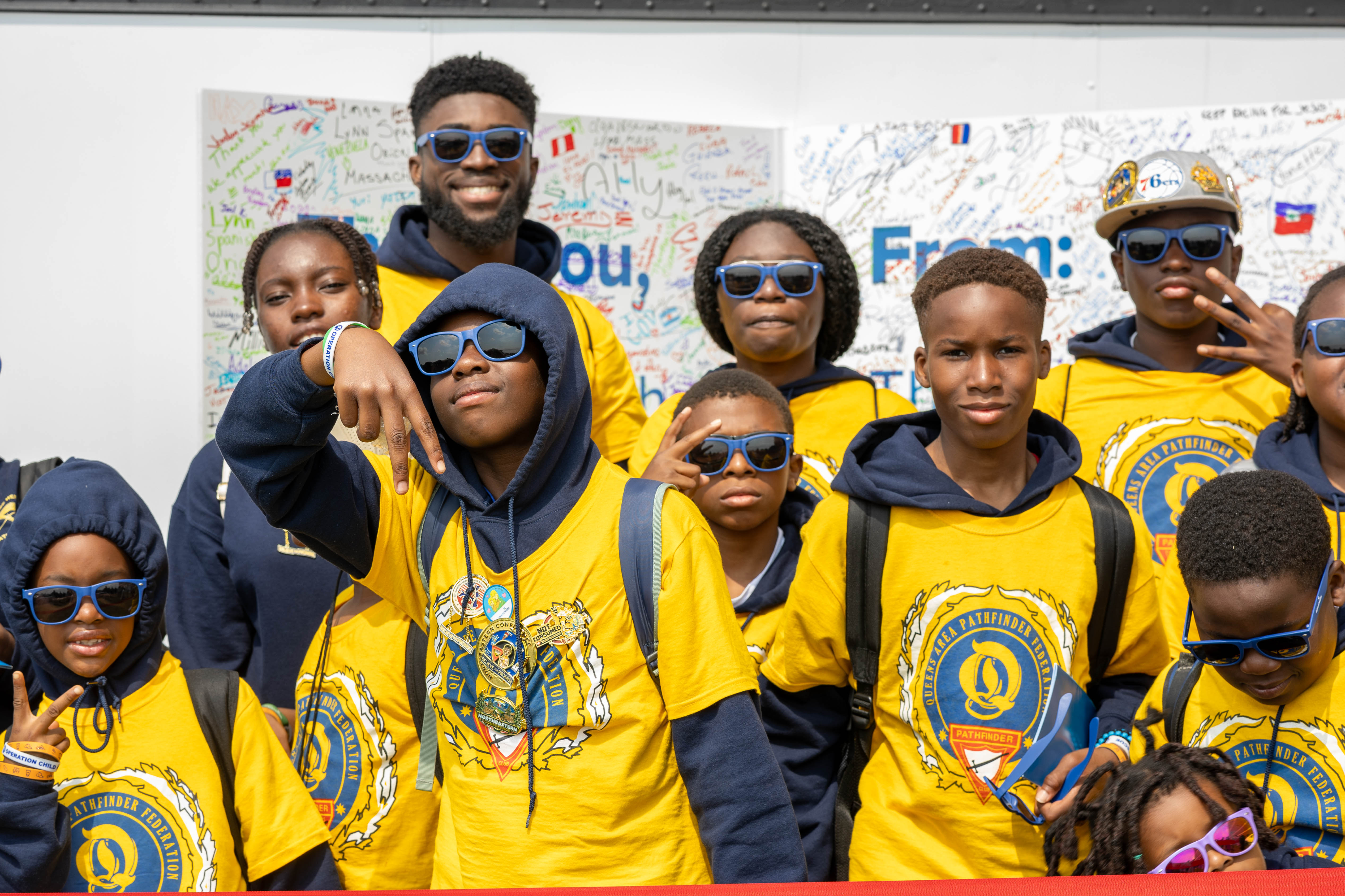 A group of young people in yellow Pathfinder shirts stand in front of a huge Thank You card