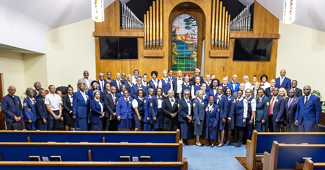 A group of people stand in front of a church in nmostly matching blue outfits.