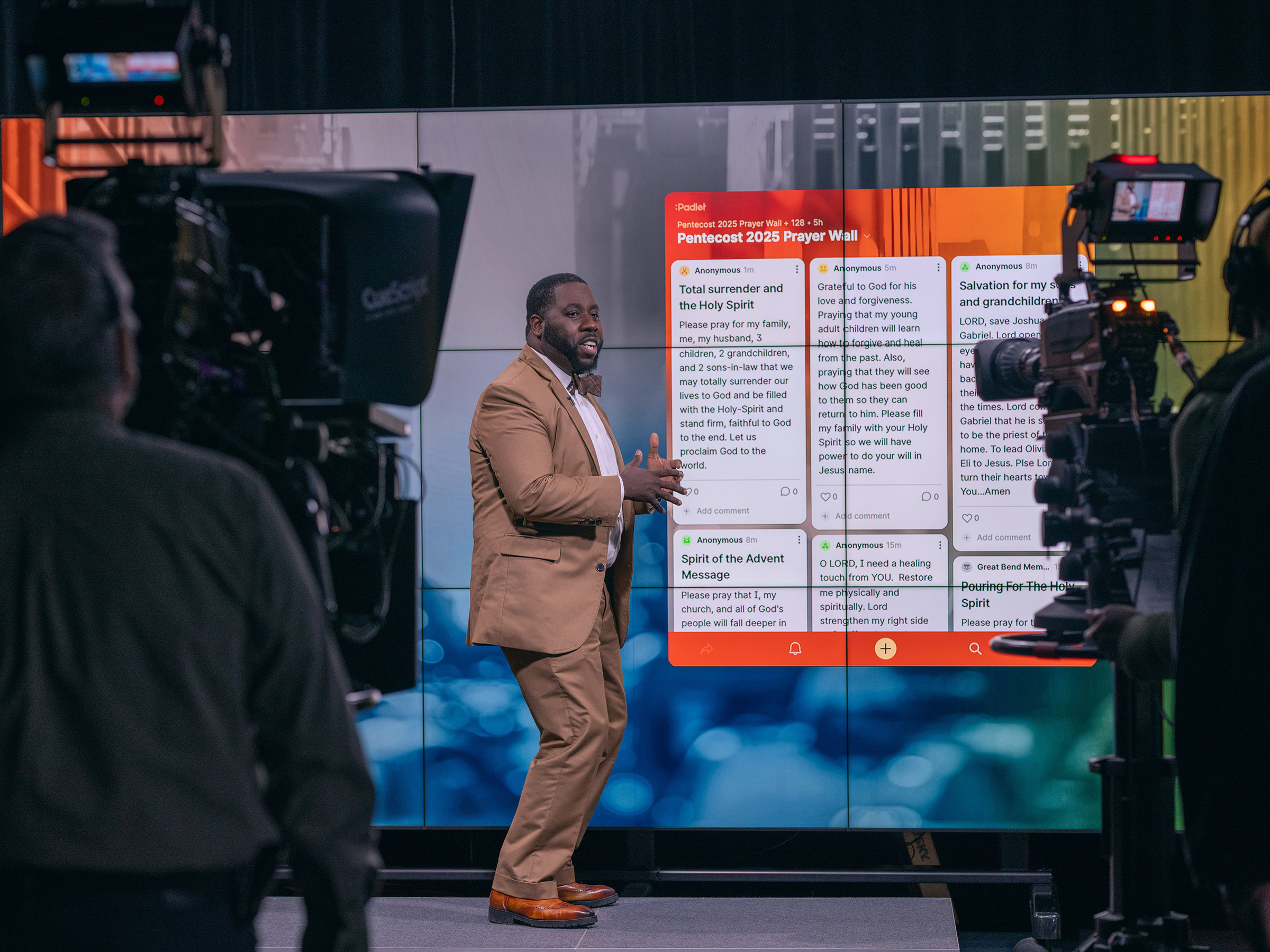 Black man in a brown suit stands in front of a digital prayer wall