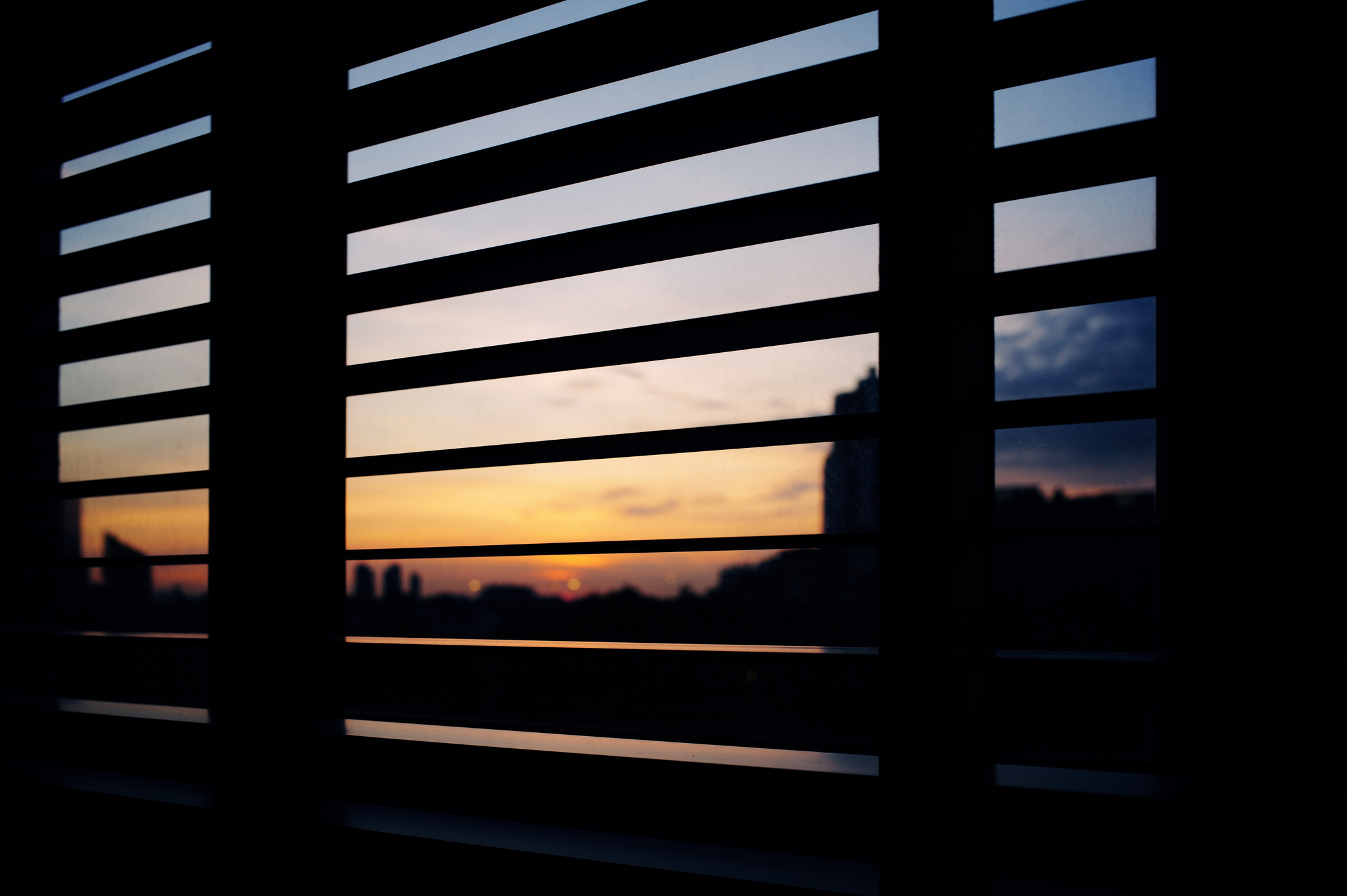 stock photo of a cityscape at dusk as seen through the blinds on a window