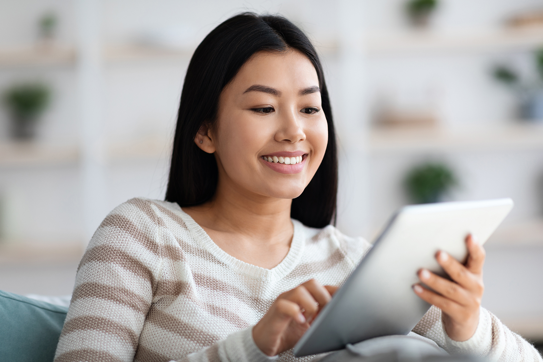 Smiling Asian woman looks at a tablet. 