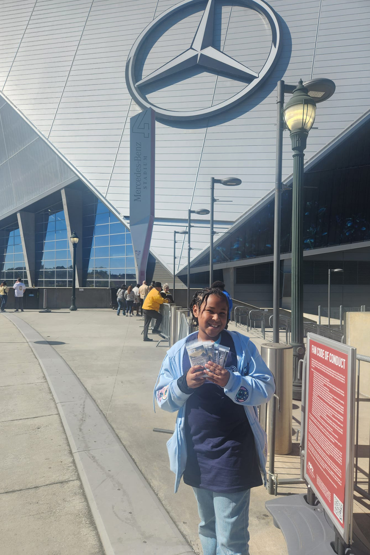 A smiling young girl holds several tracts in front of the Mercedes Stadium in Atlanta.