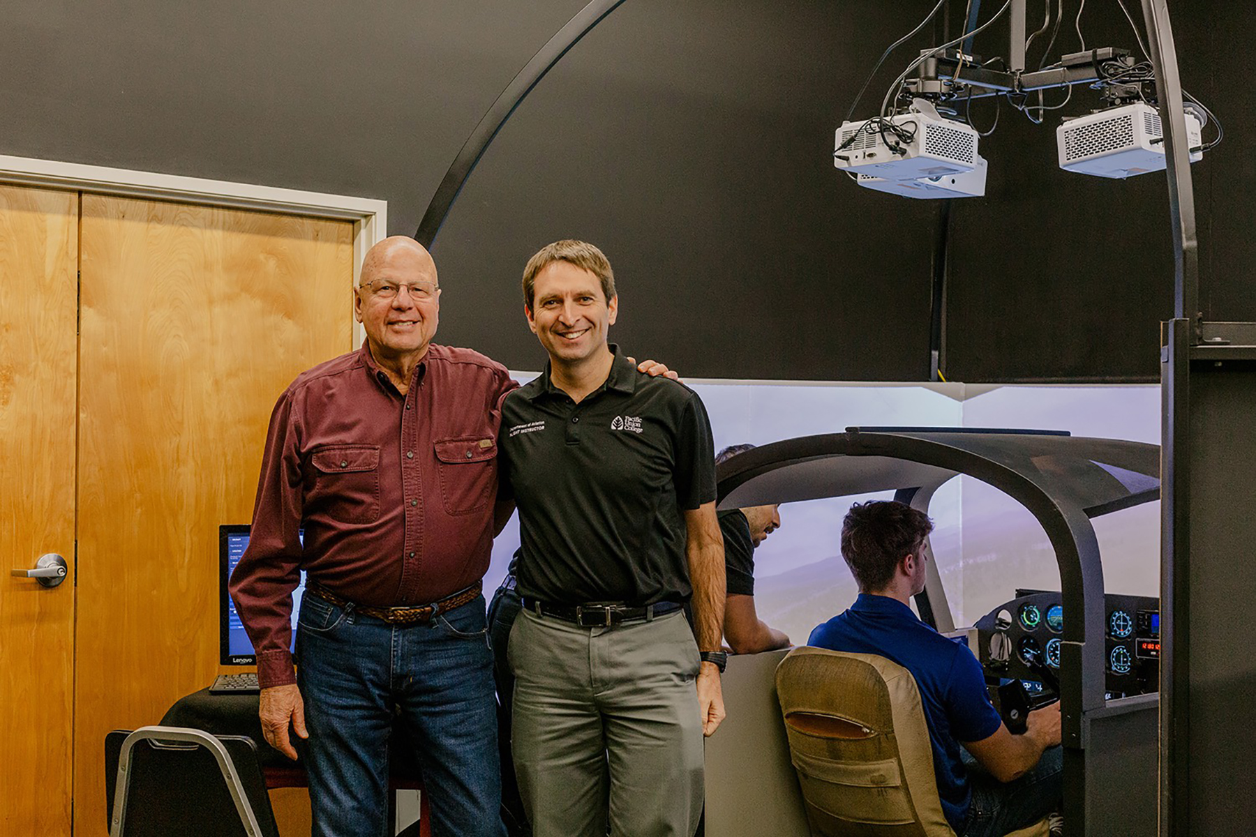 der man and younger man stand together in an aircraft simulator. 