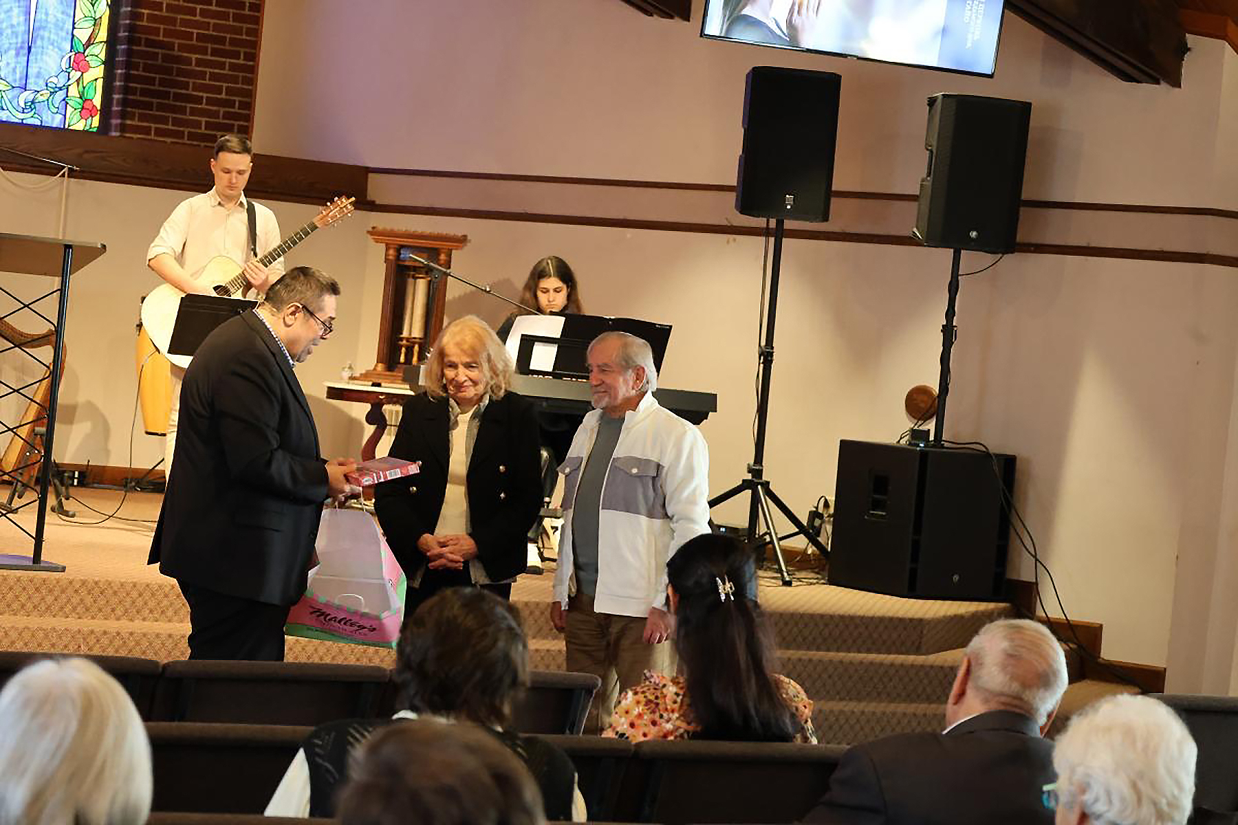 A pastor gives a gift to an elderly couple at the front of a church