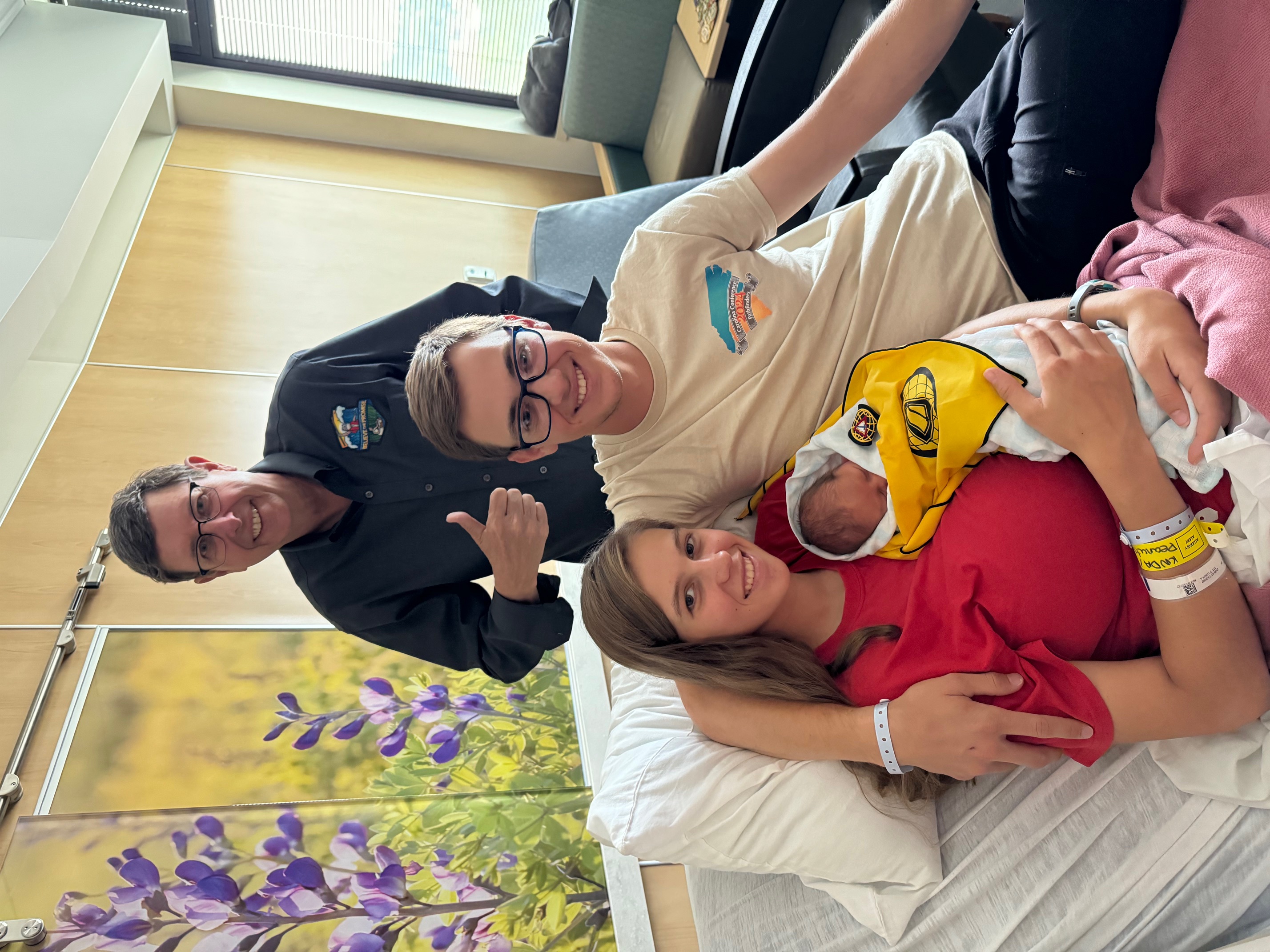 Young adult couple with their newborn baby born during the 2024 Pathfinder camporee in Gillette, Wyoming, posed with middle aged man