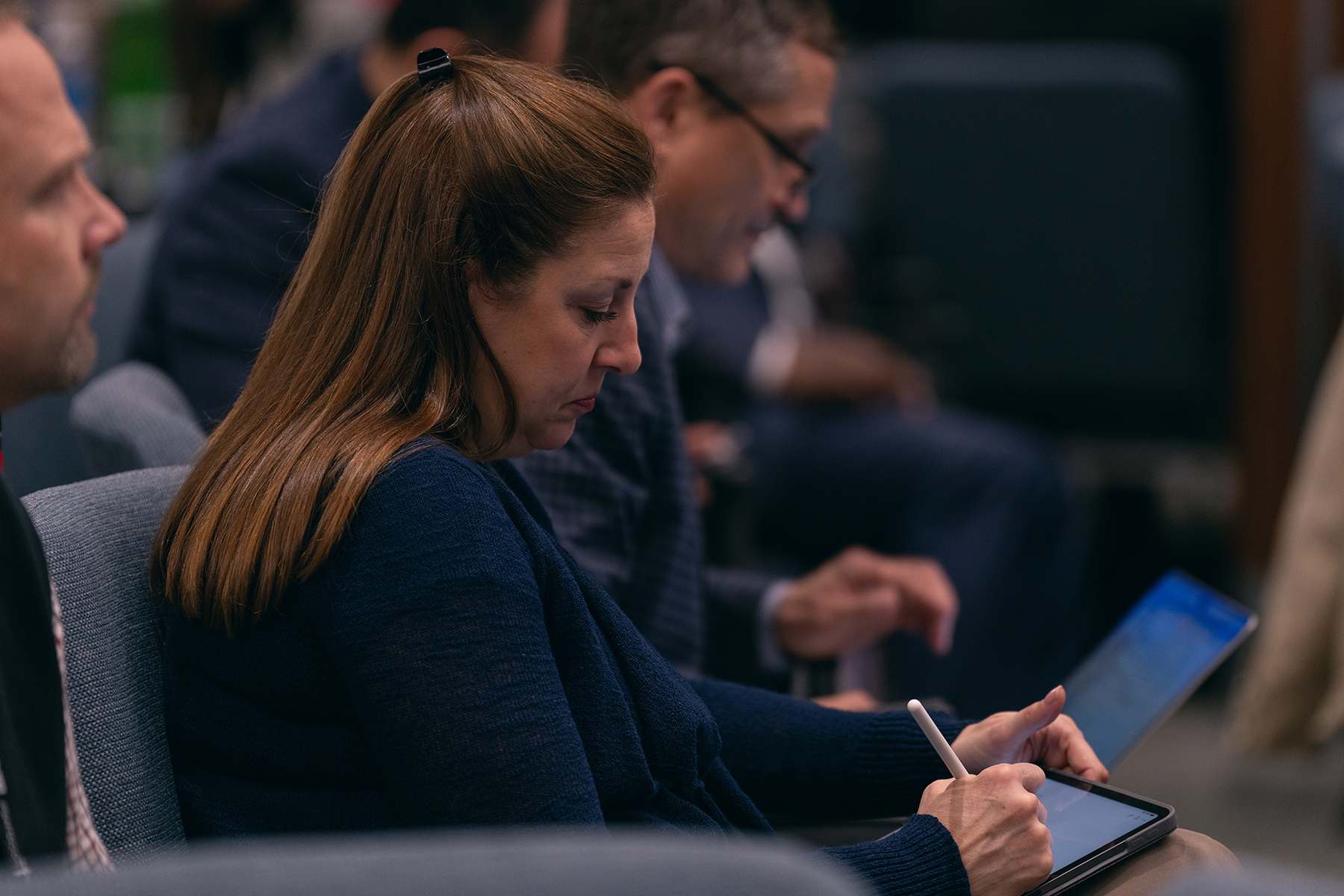 A woman at a conference writes on a tablet. 