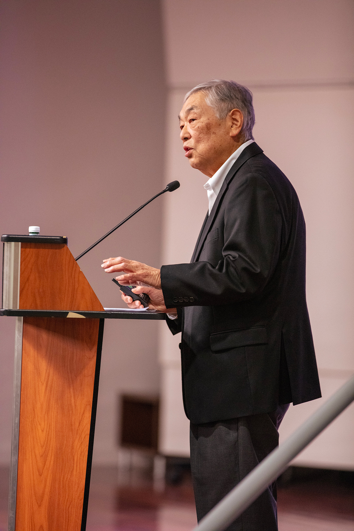 An Asian man stands behind a podium, speaking