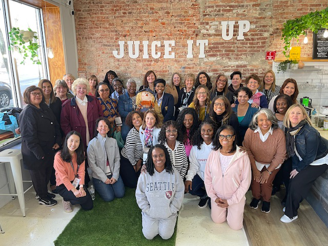 A group of women take a photo inside a cafe with the words "Juice it Up" on the wall