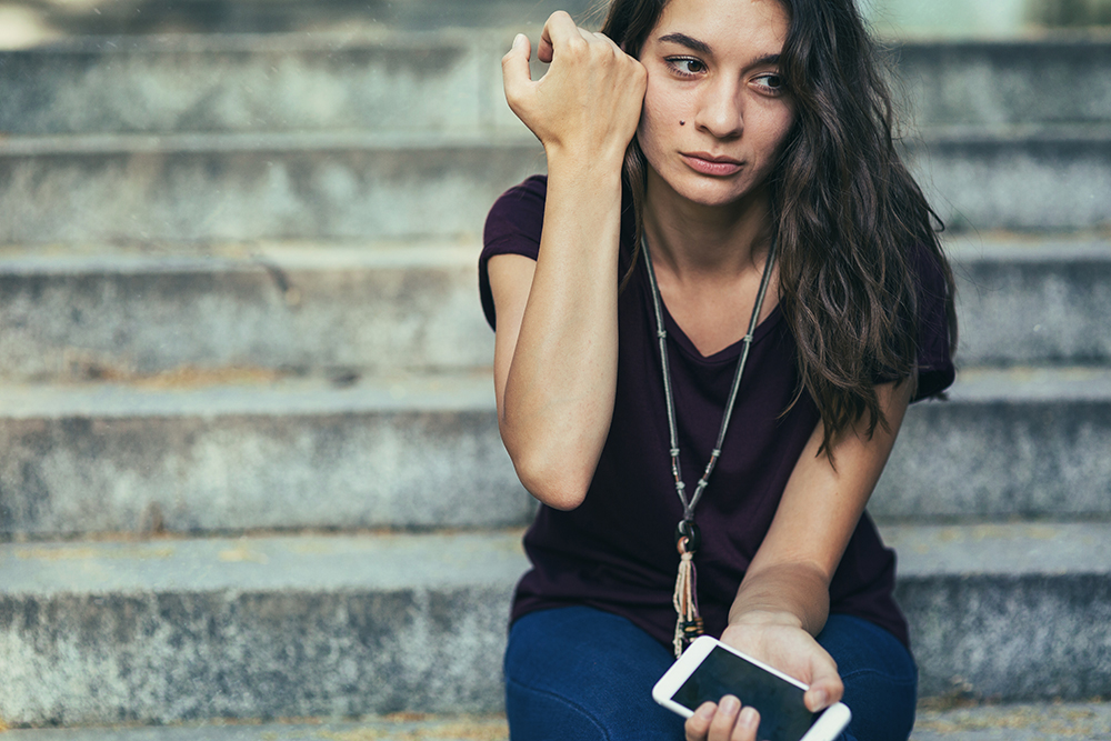 Young woman sitting on steps crying with cell phone in hand