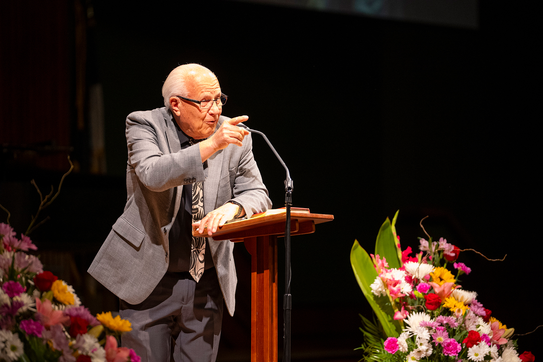 Close-up of an older man speaking on a stage, pointing his finger