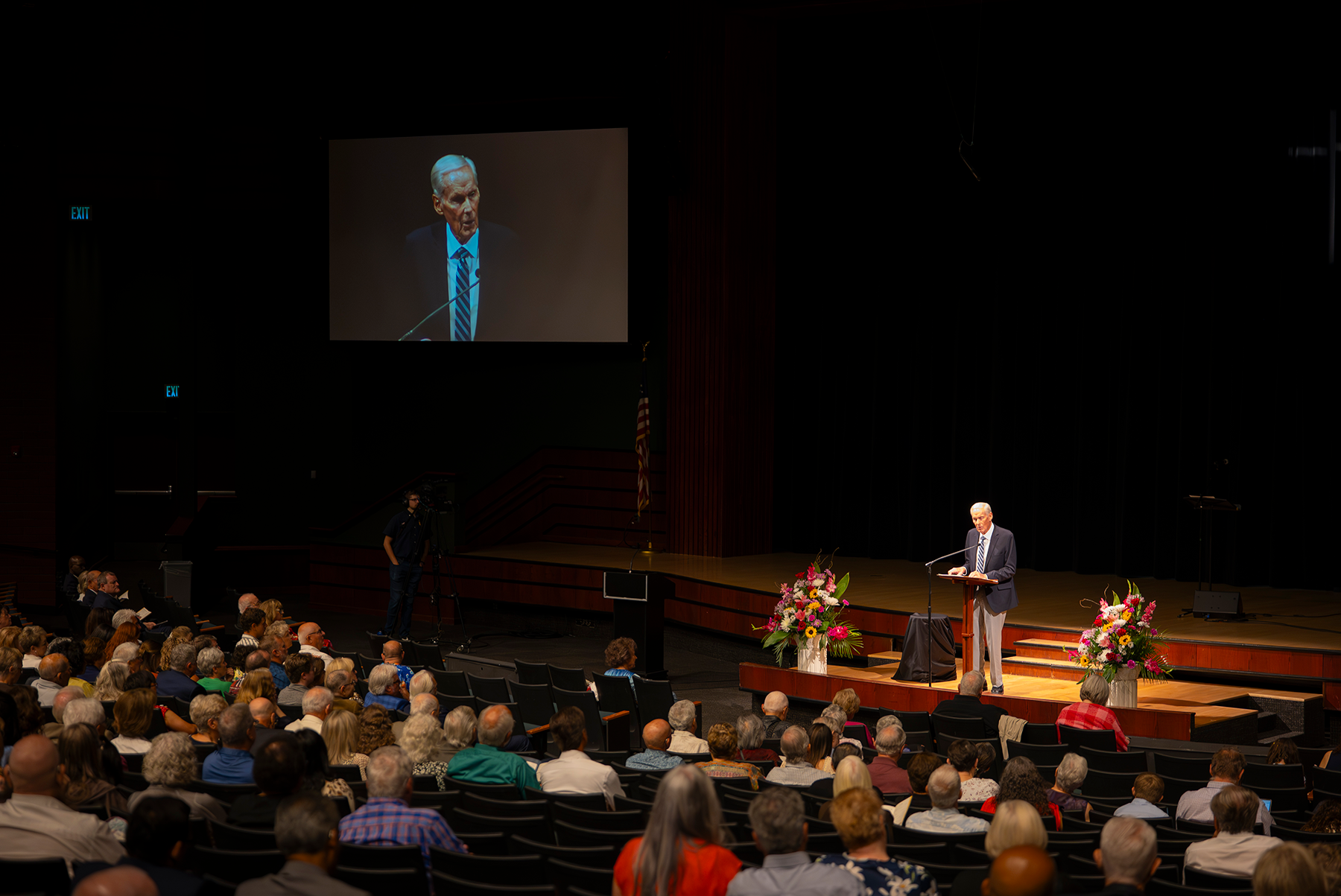 Photo of an older man on stage in front of a large group of people