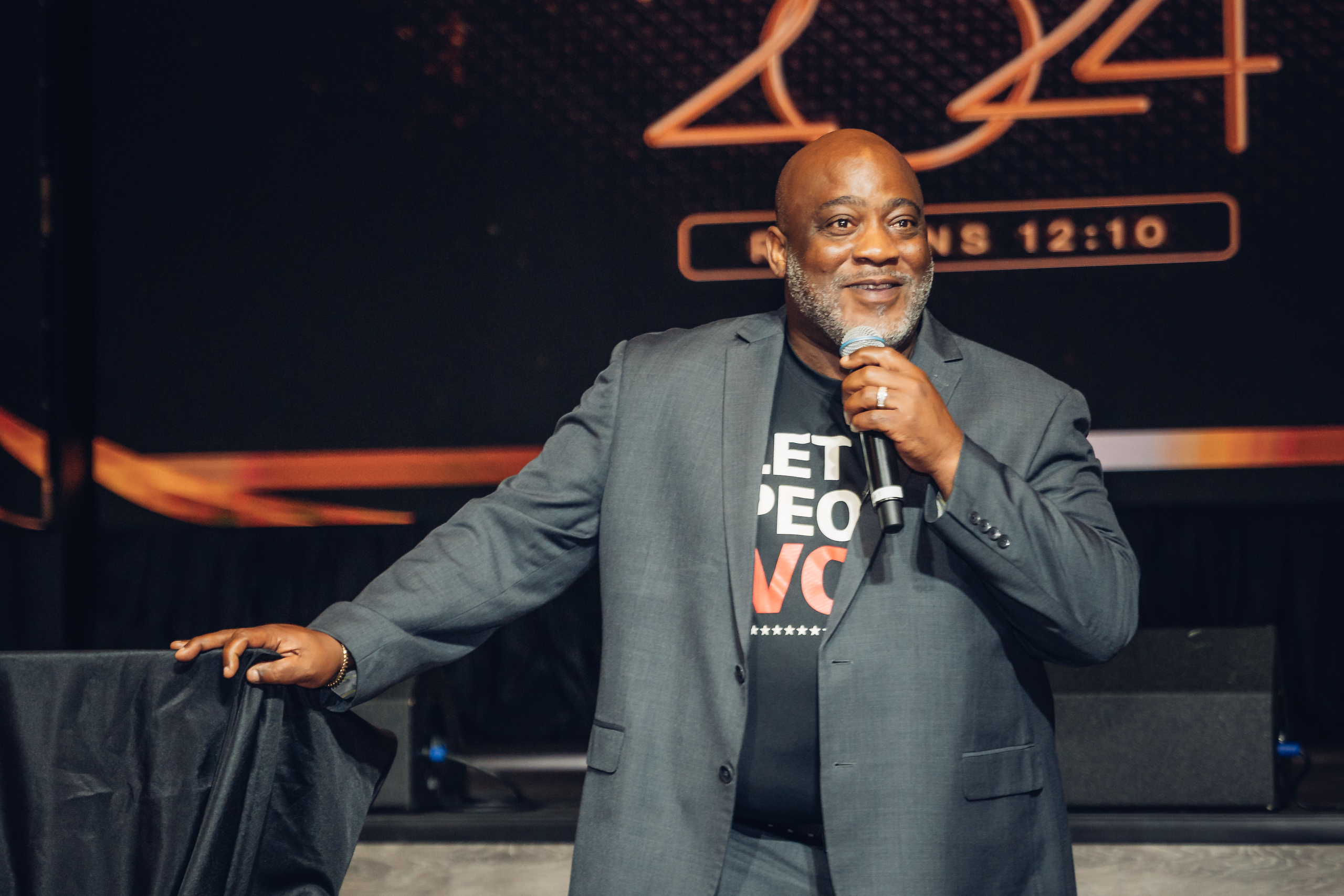 A smiling black man speaks in front of a crowd.