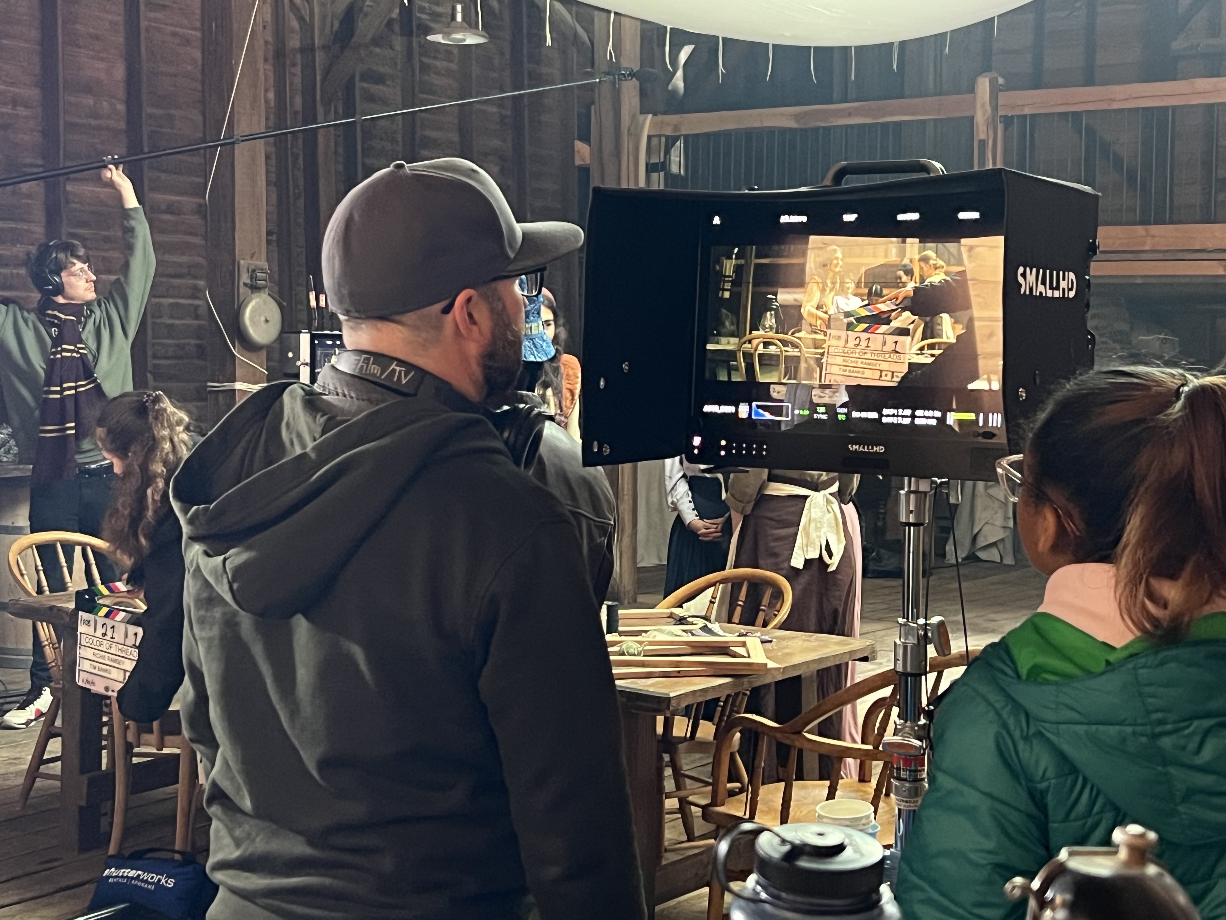 A man and woman look into an on-camera monitor at women being filmed on set. 