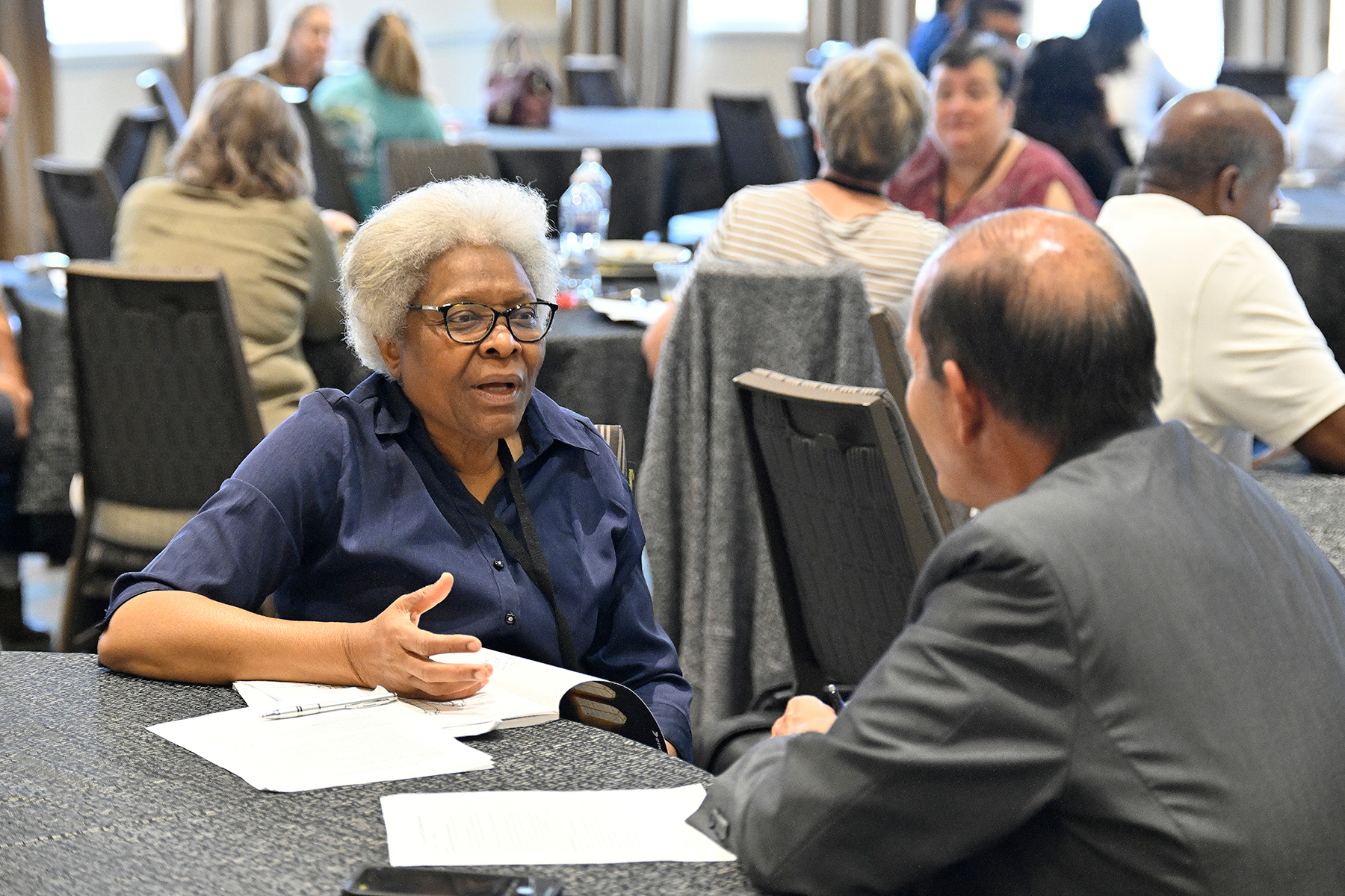 A black woman speaks to a Hispanic man in a conference room.