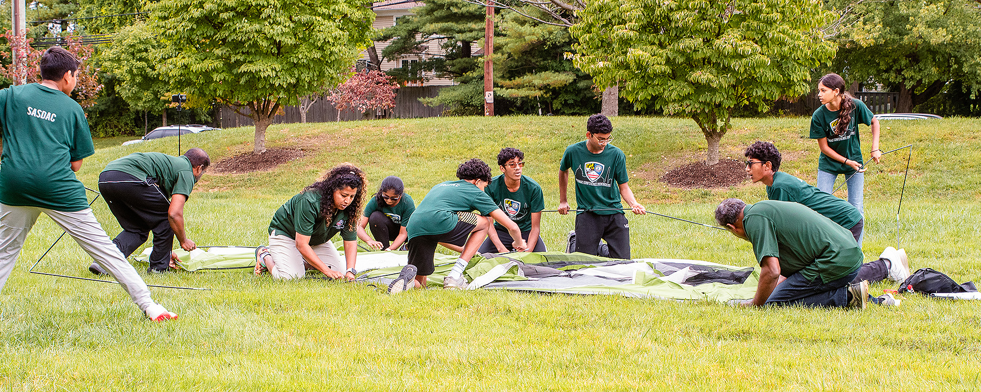 Young people pitch a tent on a grassy plain.