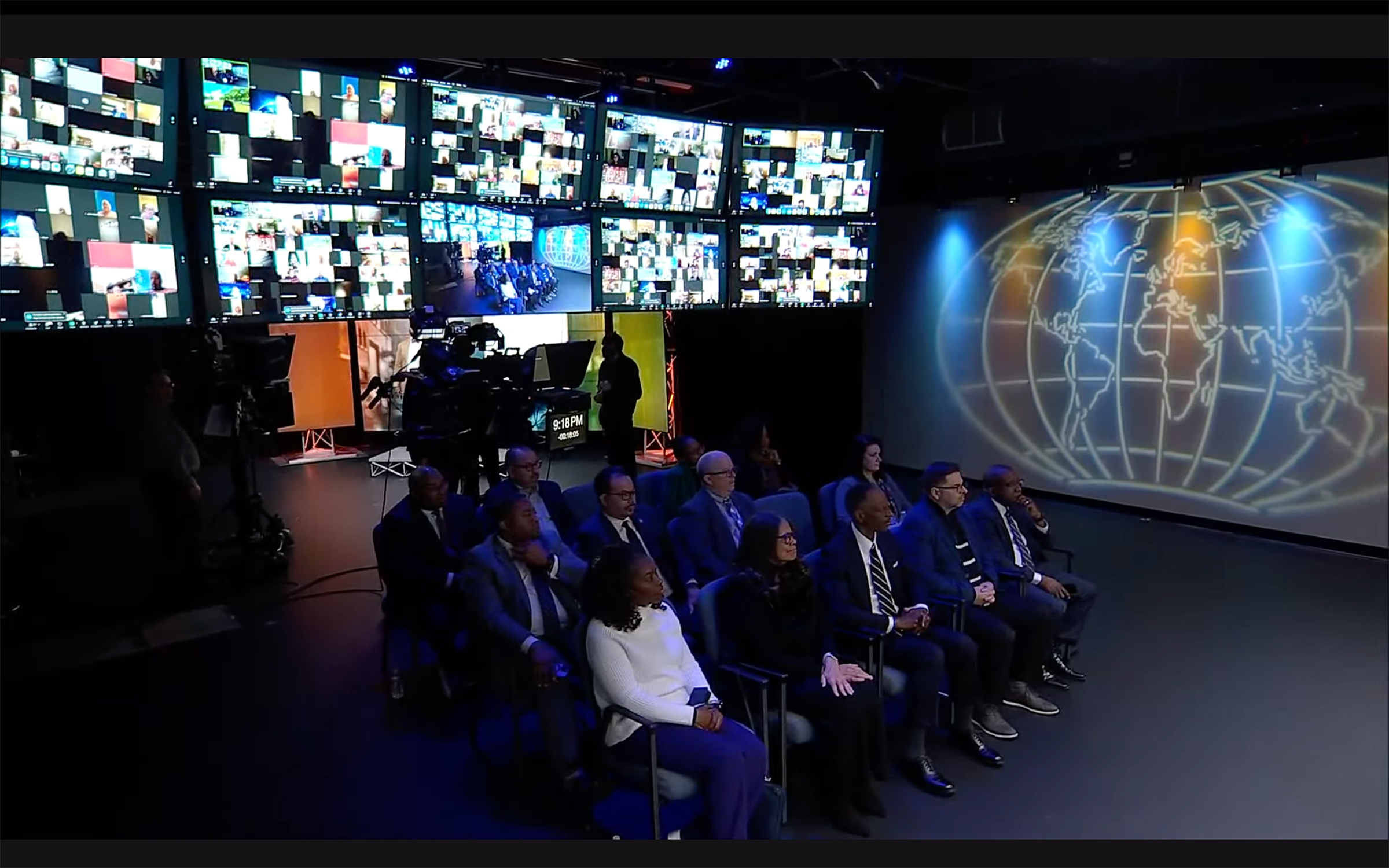 Screenshot of in-person audience and global audience on several screens behind them